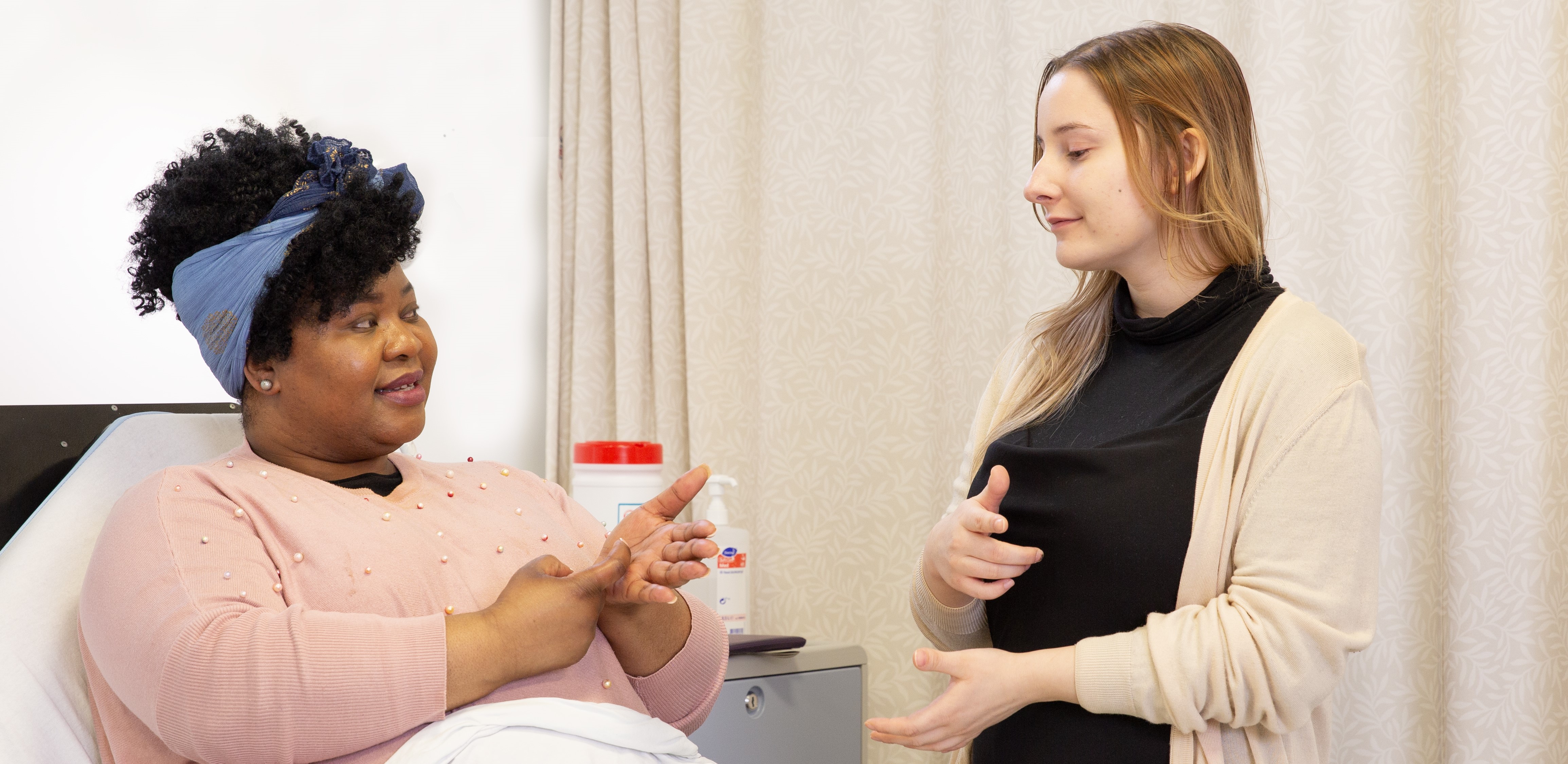 Woman in bed using sign language to talk with another woman.