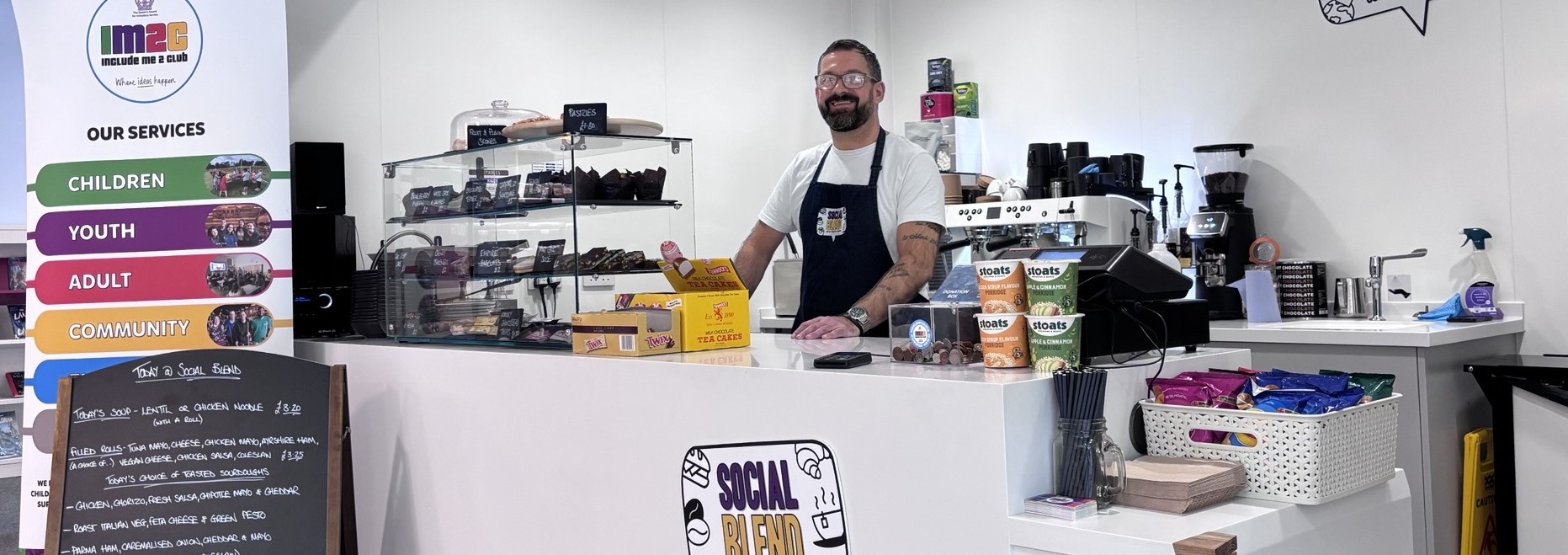 Social Blend cafe. Man standing behind counter of food.